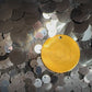 Auric Illumination Disc. Yellow circular pendant with intricate design on a background of silver sequins