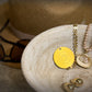 Auric Illumination Disc. Jewelry set including a yellow pendant, necklace, and earrings on a stone surface.