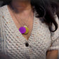 Auric Illumination Disc. Necklace with purple and gold pendants worn by a person in a textured sweater.